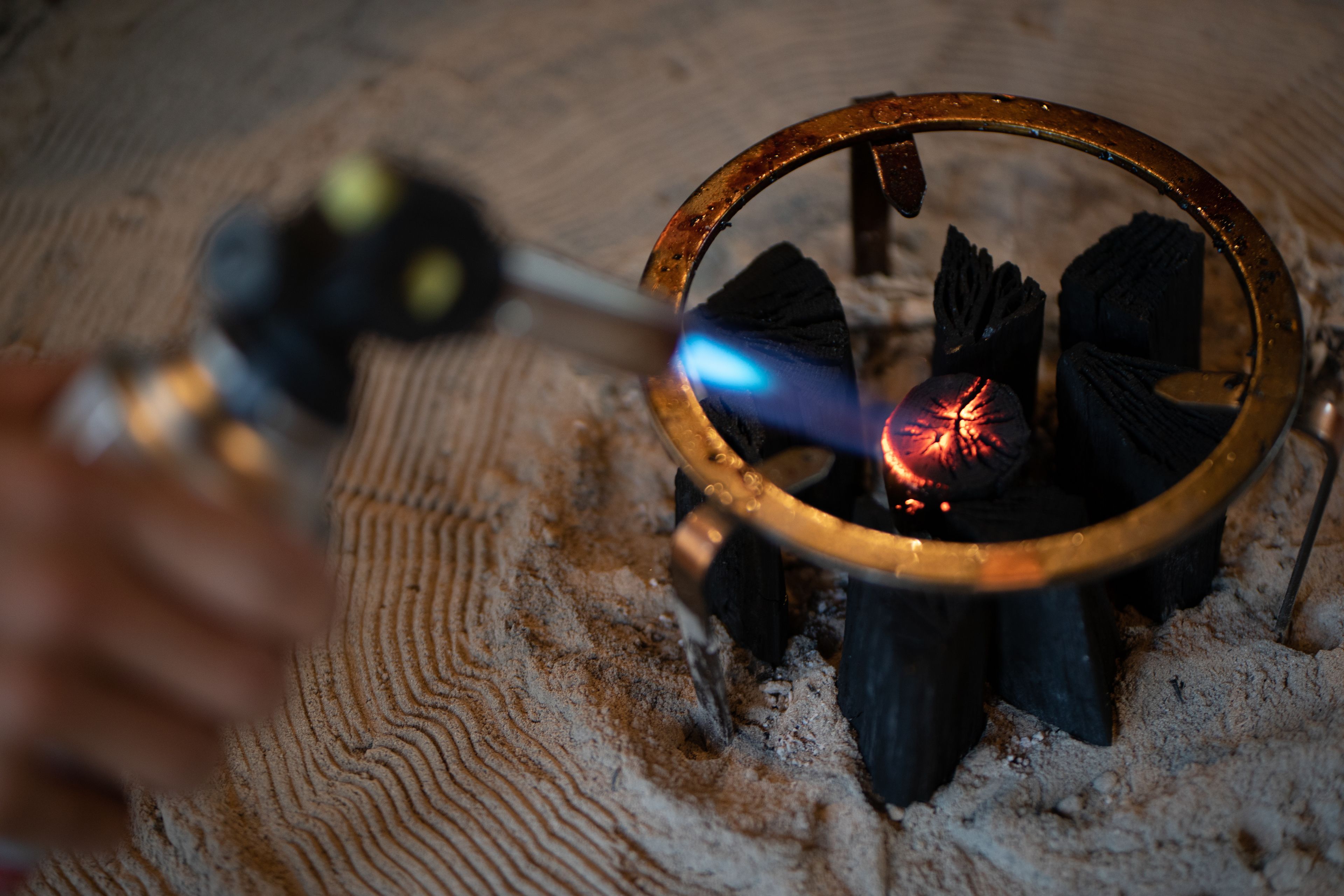 A close-up of a circular metal frame with a glowing ember inside, surrounded by a sandy surface.