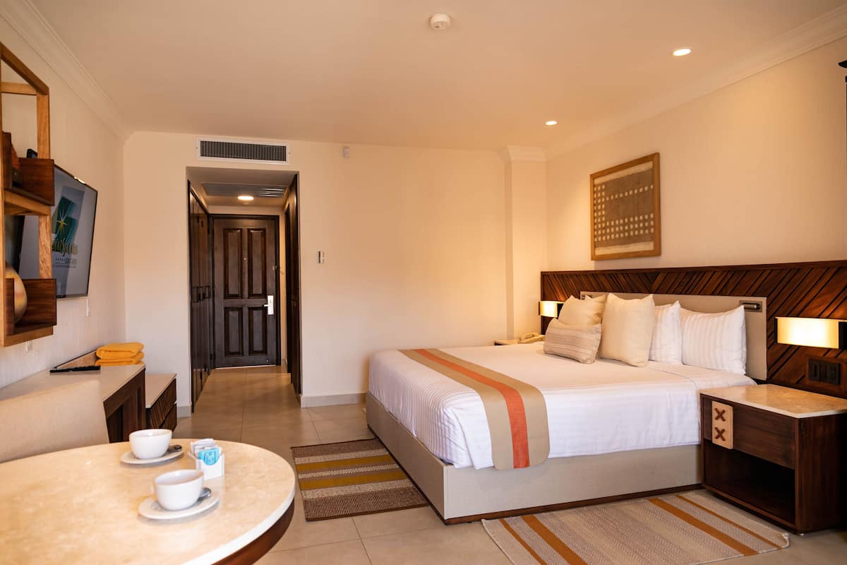 A hotel room with a bed, bedside table, lamp, and a small table with cups and saucers.