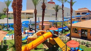 A water park with slides and play structures, surrounded by palm trees and buildings. - Club Solaris Los Cabos (San José del Cabo)