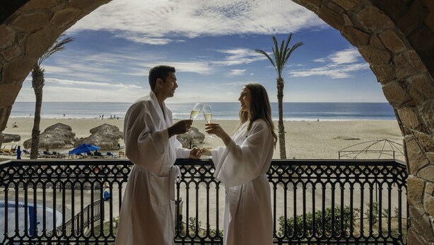 A stone archway overlooking a beach with a couple toasting with champagne glasses. - Club Solaris Los Cabos (San José del Cabo)