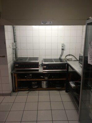 A compact kitchen with two electric ranges, a sink, and a stainless steel countertop. - Market Tavern - Hostel and Bar (South Melbourne)