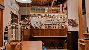 Un área de bar rústica con estantes de madera llenos de varias botellas y un gran contenedor metálico con la etiqueta 'MINTAGE'.