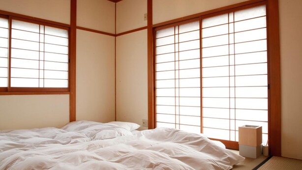 Una habitación tradicional japonesa con suelo de tatami, cama con ropa blanca y puertas correderas shoji.