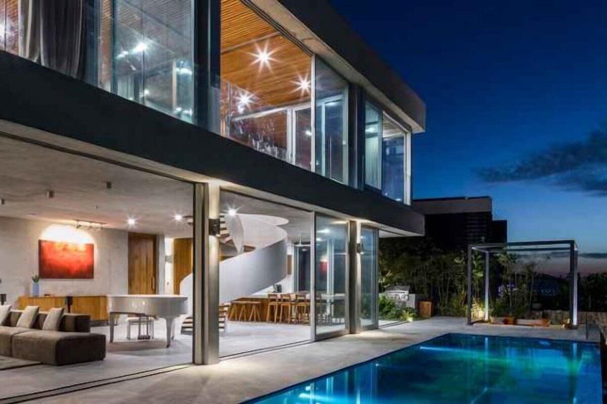 Ett modernt hus med en swimmingpool, ett matområde och en trappa som leder upp till övervåningen.