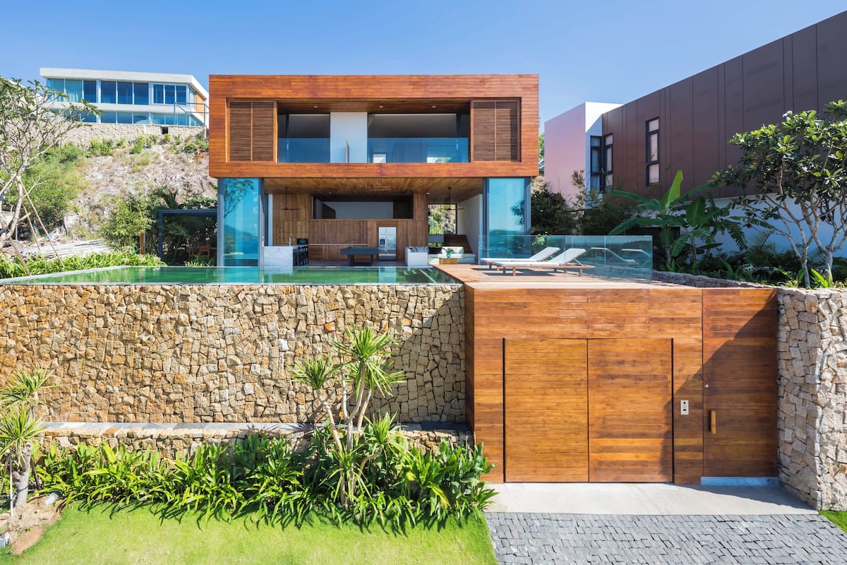 Une maison moderne avec un mur en pierre, une piscine et une terrasse en bois.
