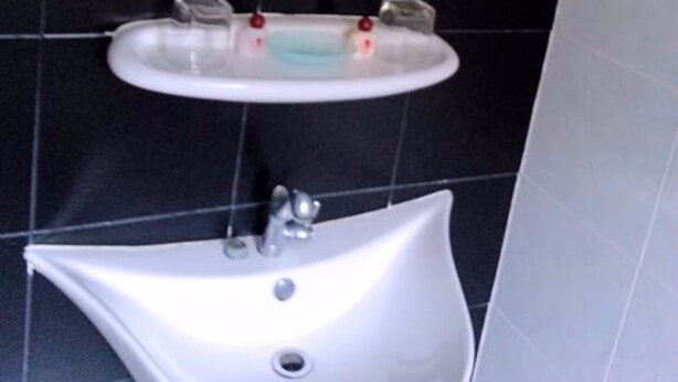 A bathroom with a white sink, a mirror, and black tiled walls. - Fong Kaew and Baan Nang Fa Guesthouse (Patong)