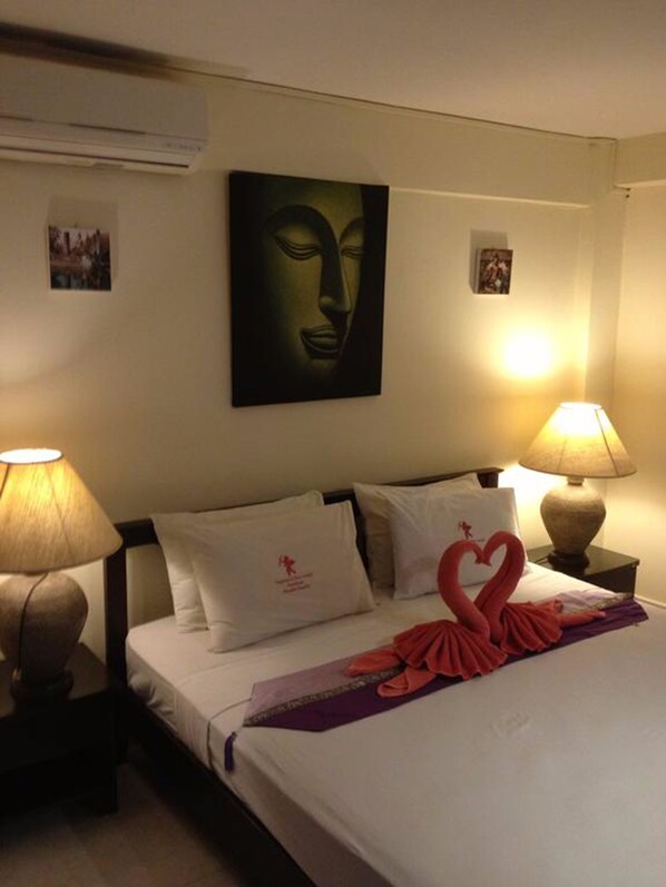 A hotel room with a bed, two bedside lamps, a wall-mounted air conditioner, and a painting above the bed. - Fong Kaew and Baan Nang Fa Guesthouse (Patong)