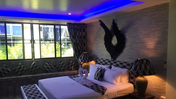 Ein modernes Schlafzimmer mit einem großen Bett, gemusterten Kissen, einer Wanddekoration und einem Fenster mit Vorhängen.