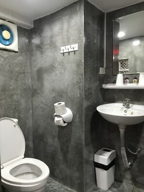 A bathroom with a toilet, a sink, a trash bin, and a toilet paper holder. - Fong Kaew and Baan Nang Fa Guesthouse (Patong)