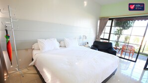 Un cuarto de hotel con una cama grande, una silla, un escritorio con lámpara y vista al exterior a través de un ventanal amplio.