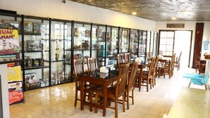 Un restaurante con vitrinas de vidrio exhibiendo diversos artículos, mesas y sillas de madera, y suelo de baldosas.