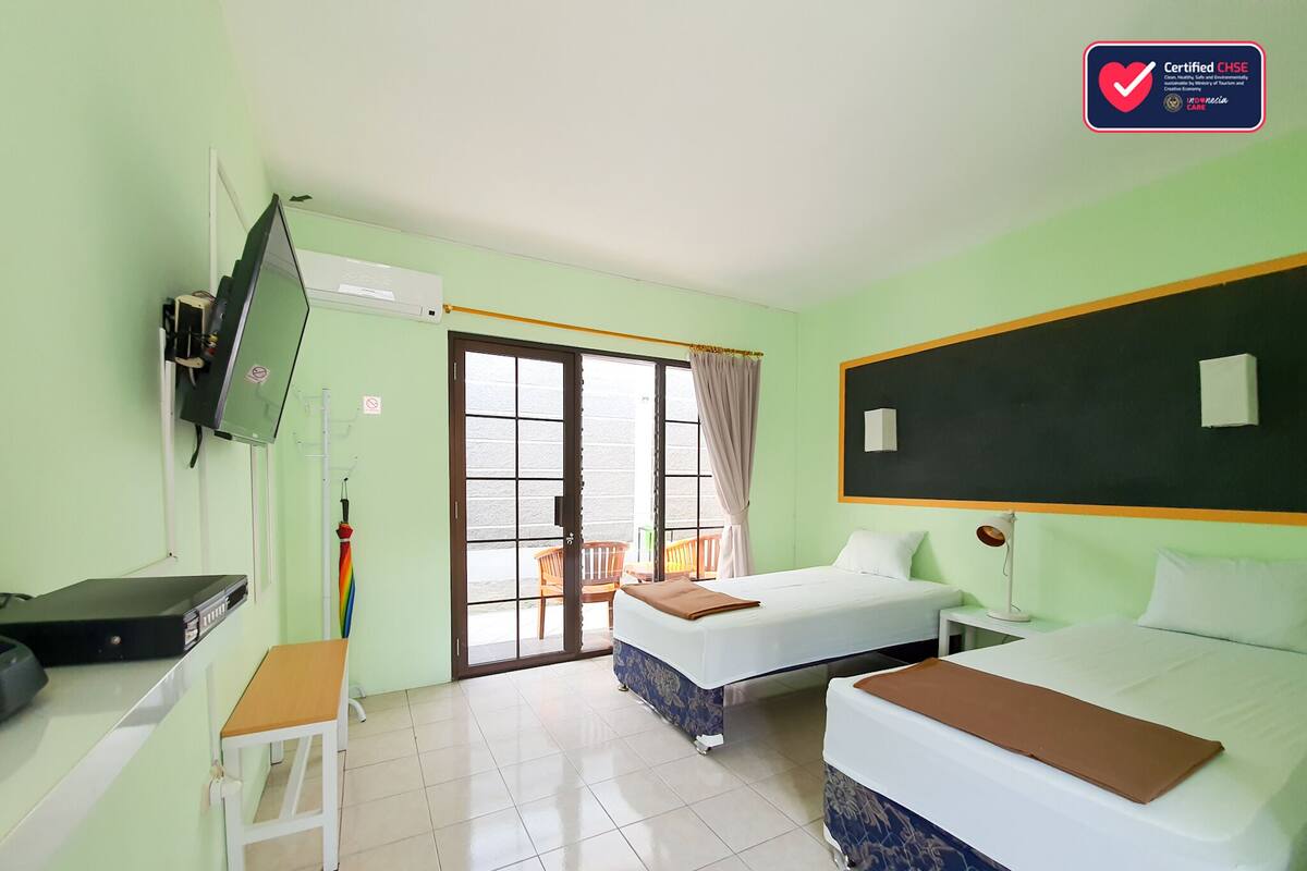 A hotel room with two beds, a desk, a television, and a window with a view of the outside.