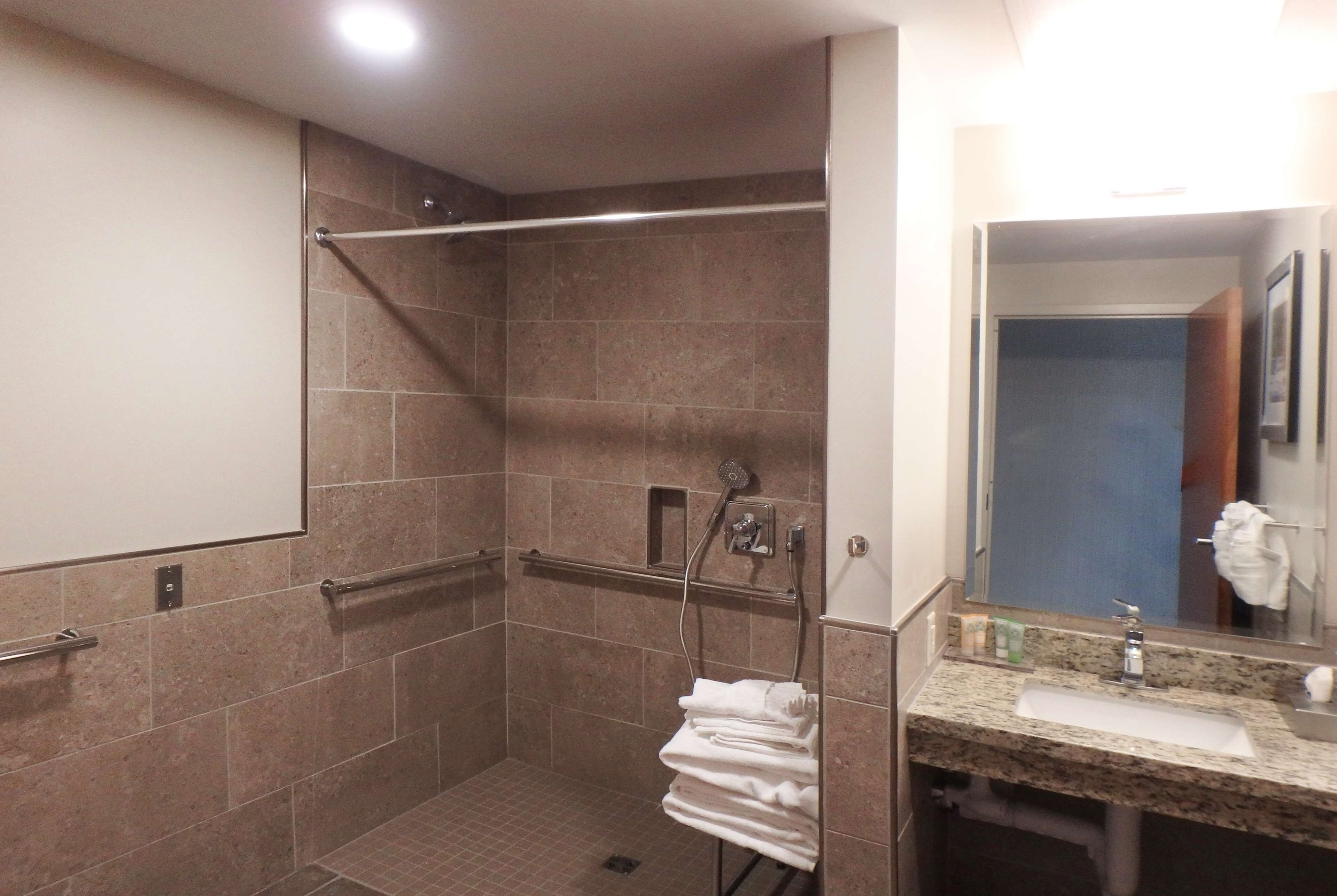 A bathroom with a shower, grab bars, a towel rack, and a sink with a mirror.