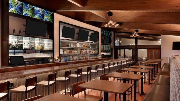 A restaurant with a long counter, multiple TVs, and a variety of seating options including tables and benches. - Wyndham Garden State College (Boalsburg)