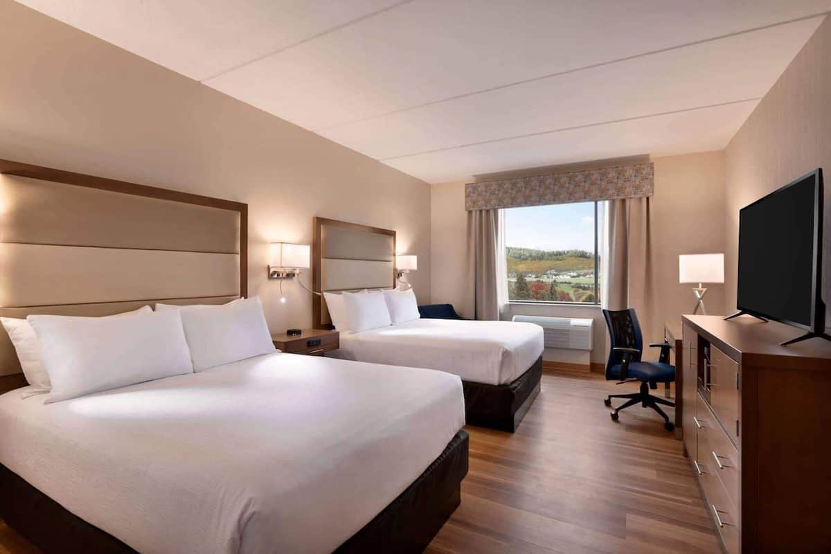 A hotel room with two beds, a television, a desk, and a view of the countryside.
