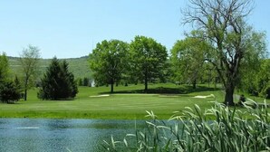 A serene golf course with a pond, trees, and a clear sky. - Wyndham Garden State College (Boalsburg)