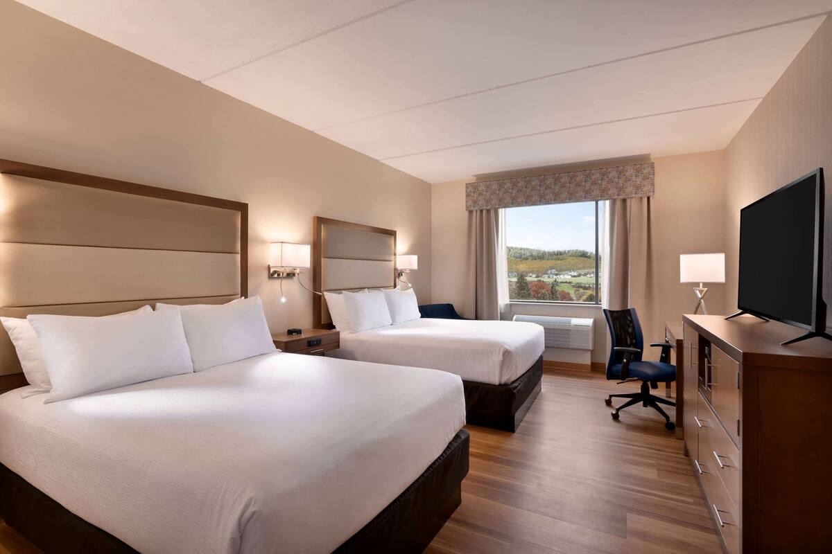 A hotel room with two beds, a desk, a chair, a TV, and a window with a view.