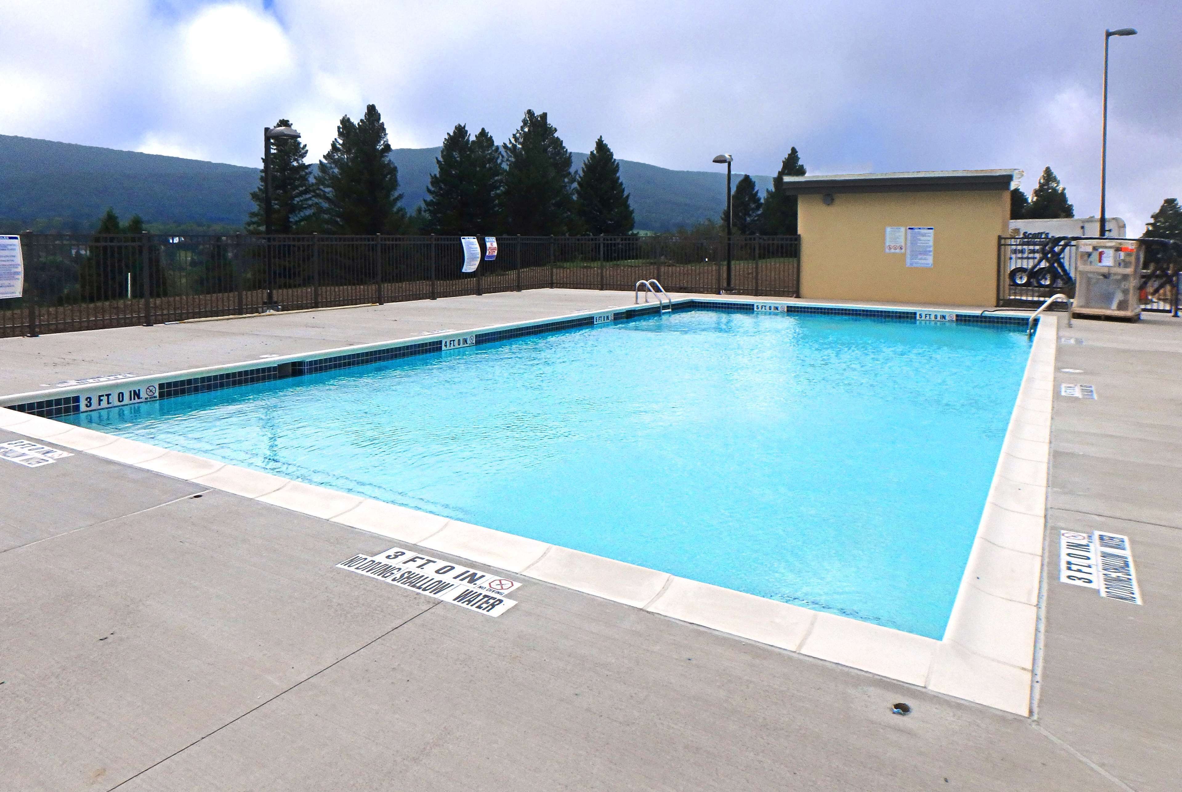 Una piscina rectangular con agua cristalina azul, rodeada por un solárium de hormigón. Se observan señales que indican la profundidad y zonas donde no se permite bucear.