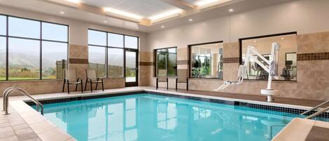 A swimming pool with clear blue water, large windows, and a view of the mountains.