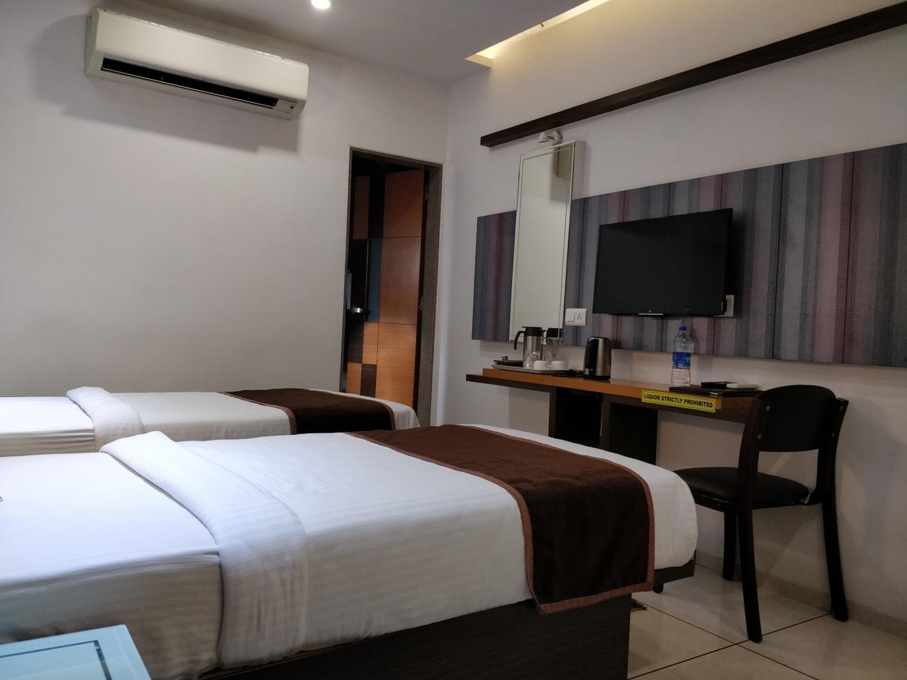A hotel room with two beds, a desk with a chair, a television, and an air conditioning unit.