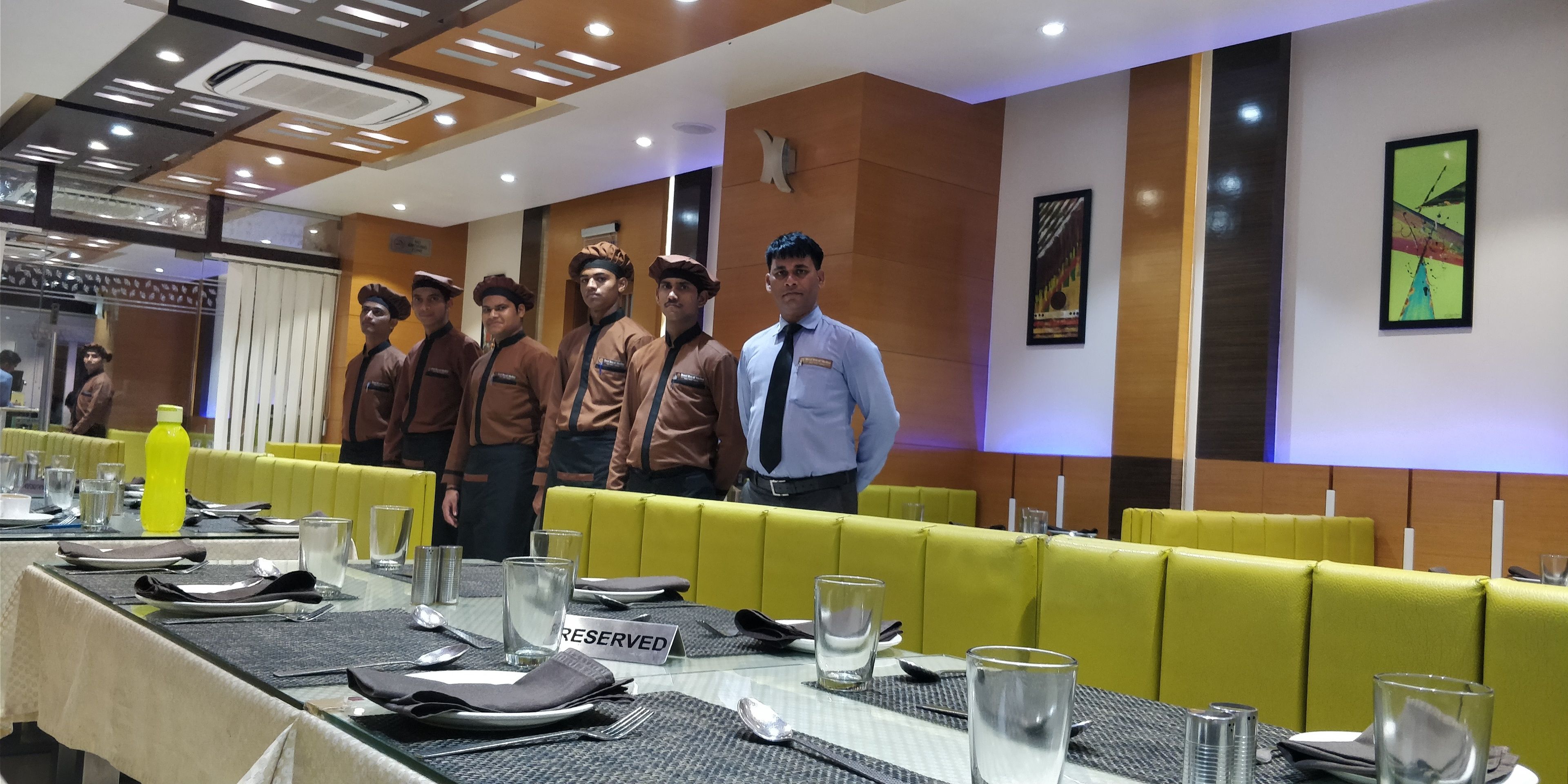A restaurant with yellow booths, a table set with plates, glasses, and cutlery, and a 'RESERVED' sign on the table.