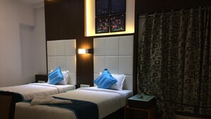 Habitación de hotel con dos camas, una mesita de noche, una pequeña mesa y una ventana con cortinas.