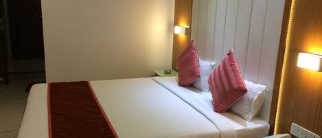 A hotel room with a bed, a bedside table with a phone, and a wall-mounted light fixture.