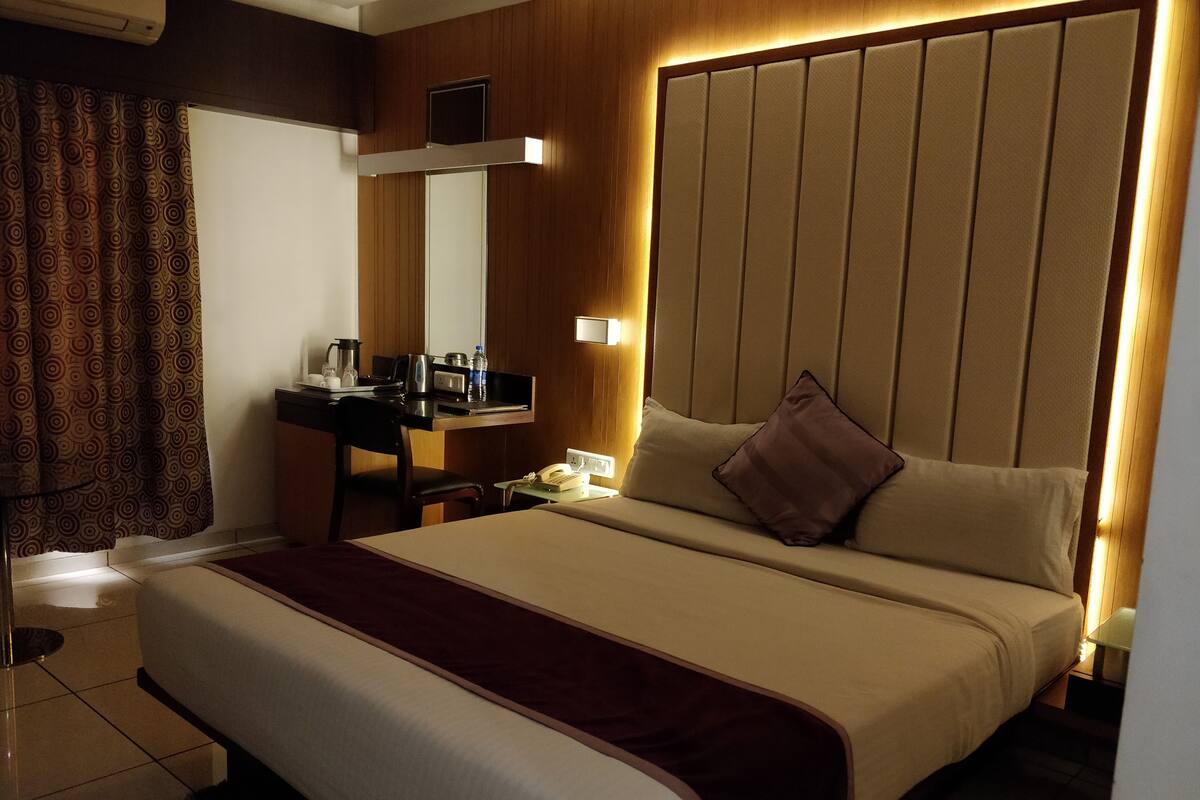 A hotel room with a large bed, a desk with a telephone, a mirror, and a window with curtains.