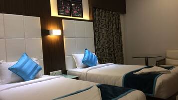 A hotel room with two beds, a nightstand, a small table, and a window with a view of the night sky.