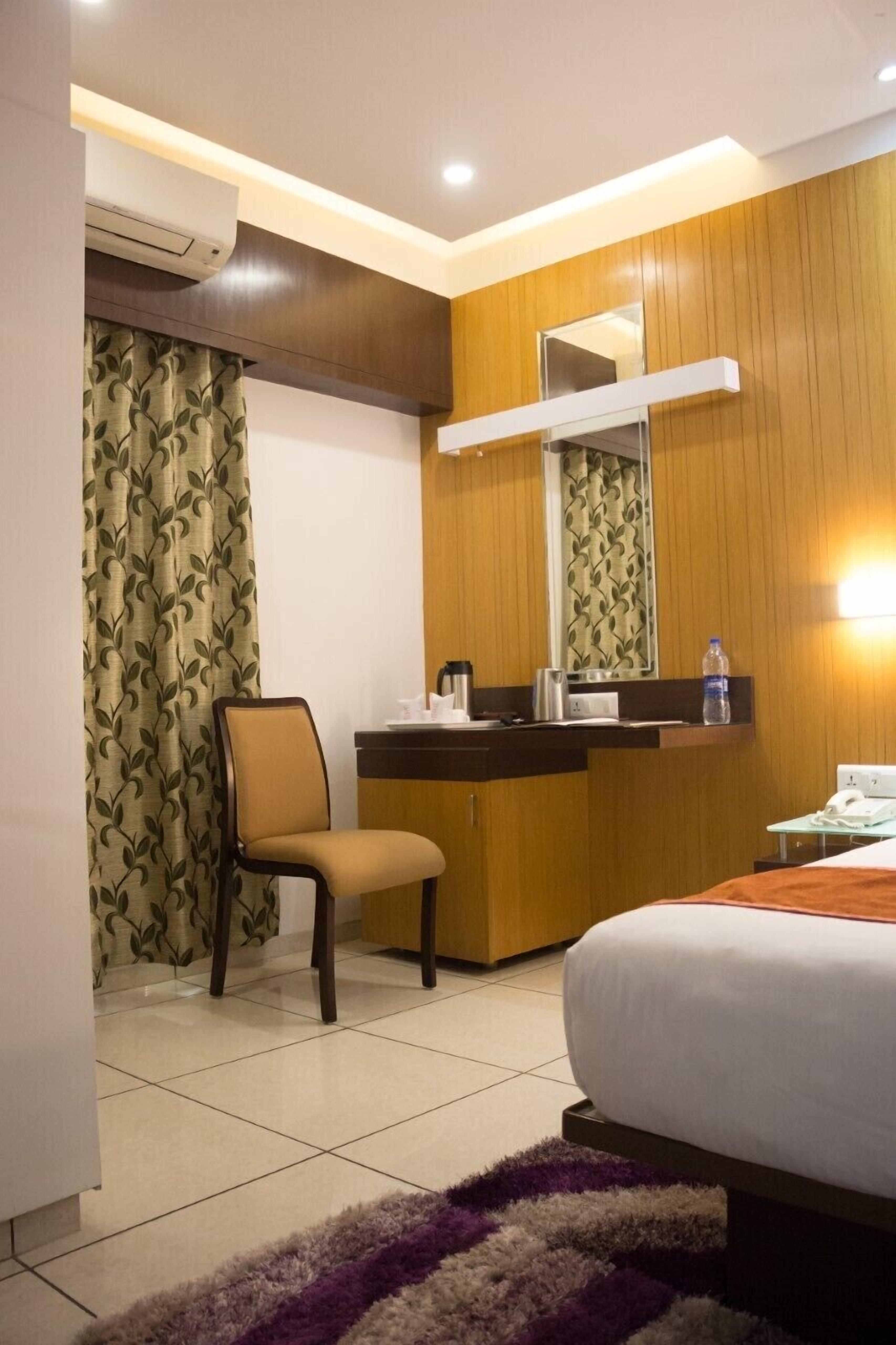 Une chambre d’hôtel comprenant un lit, un bureau avec un miroir, une chaise et une salle de bain avec un rideau de douche.