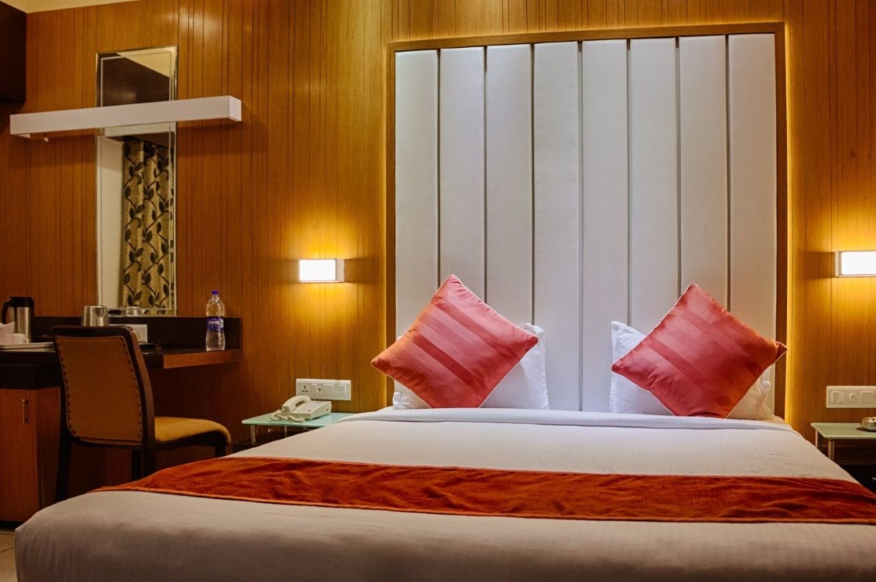 A hotel room with a bed, two pillows, a nightstand, a desk, a chair, and a mirror.
