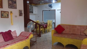 A living room with a yellow sofa and a red cushion, a dining area with yellow chairs and a table, and a kitchen in the background. - Yellow HOUSE Vacation Rental (Olongapo)