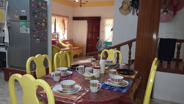 A dining area with a round table set for four, yellow chairs, and various dishes and cups. - Yellow HOUSE Vacation Rental (Olongapo)
