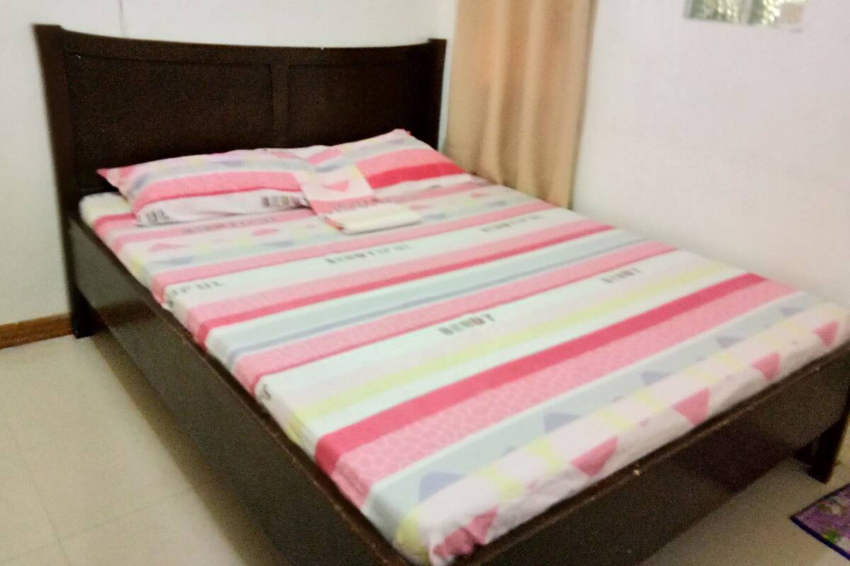 A bed with a striped bedspread and pillows, a dark headboard, and a window with curtains.
