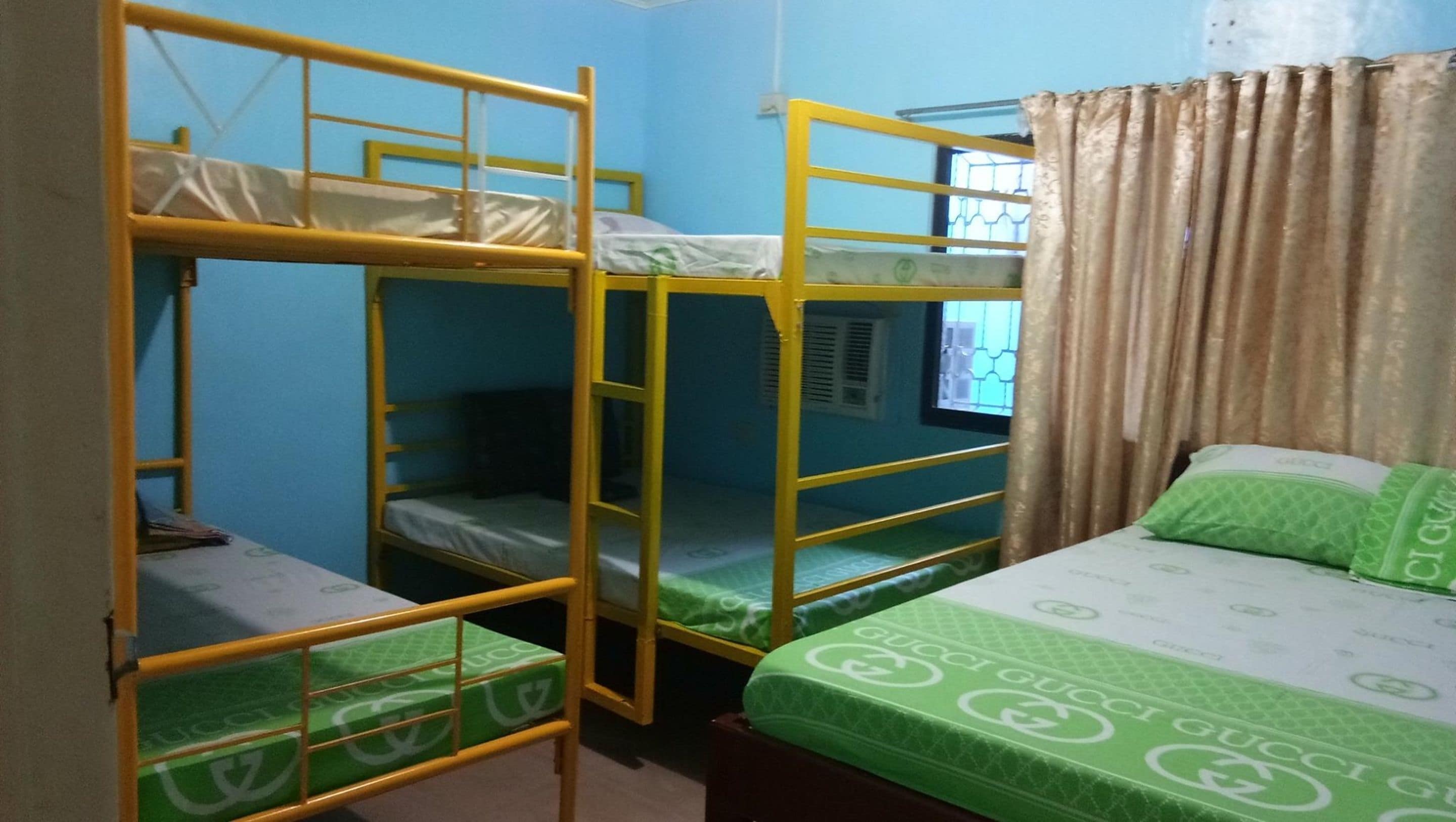 A dormitory room with bunk beds and a single bed with a green blanket.