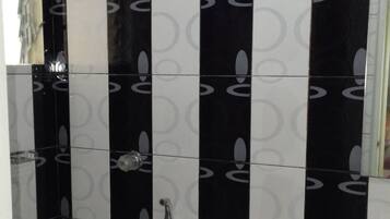 A bathroom with black and white patterned tiles, a white toilet, a yellow bucket, and a handheld showerhead.