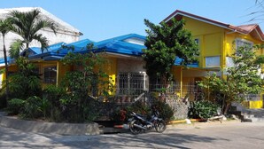 A yellow house with a blue roof, a motorcycle parked in front, and a stone wall with plants. - Yellow HOUSE Vacation Rental (Olongapo)