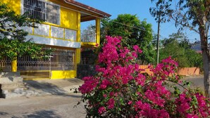 A yellow building with a balcony, surrounded by lush greenery and vibrant pink flowers. - Yellow HOUSE Vacation Rental (Olongapo)