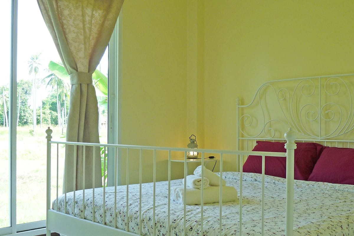 A bed with a white metal frame, a floral-patterned bedspread, and two pillows, one red and one white.