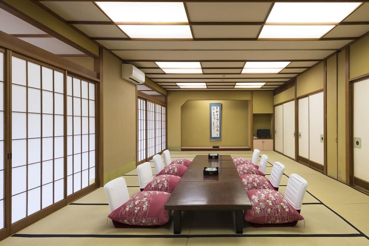 Una sala de reuniones tradicional japonesa con suelo de tatami, una mesa larga y biombos shoji.