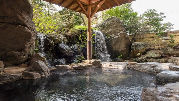 A tranquil outdoor hot spring area with a wooden pavilion, a small waterfall, and surrounding rocks. - Awazu-Spa Tourist Hotel Kitahachi (Komatsu)