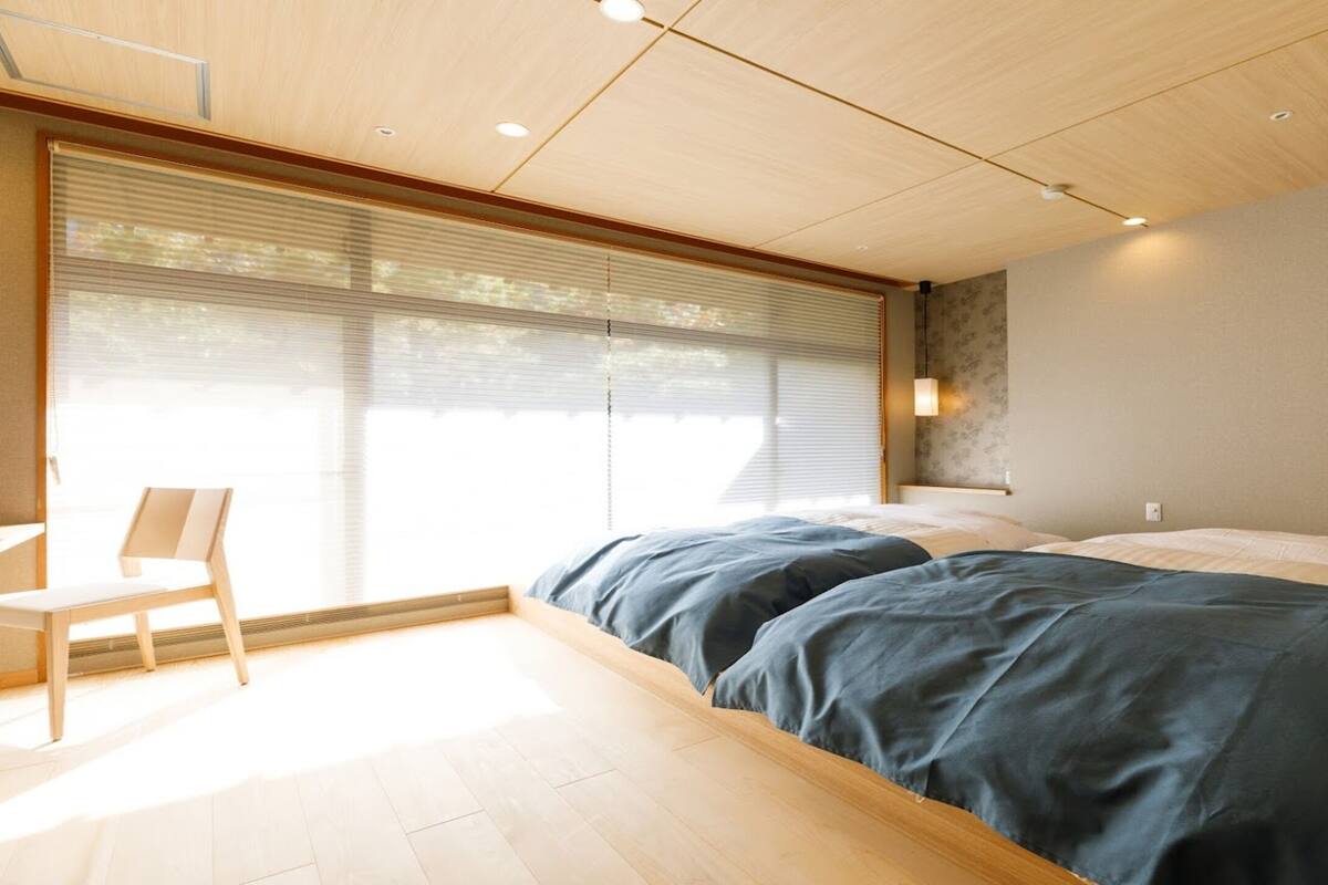 Une chambre à coucher avec un lit, une chaise et une grande fenêtre équipée de stores.