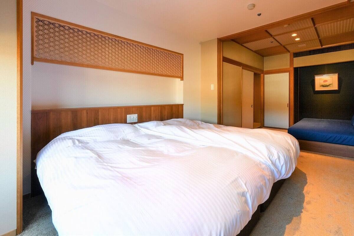 Une chambre d’hôtel avec un grand lit, un petit canapé, un panneau décoratif au mur et un tableau encadré.