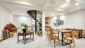 A modern dining area with wooden furniture, a spiral staircase, and a kitchen in the background. - Visut House - Hostel (Bangkok)
