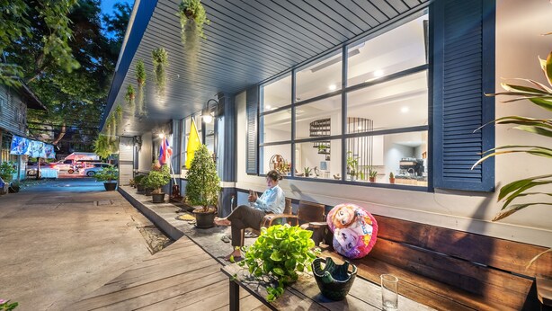A wooden deck with potted plants, a bench, and a table with a glass. - Visut House - Hostel (Bangkok)