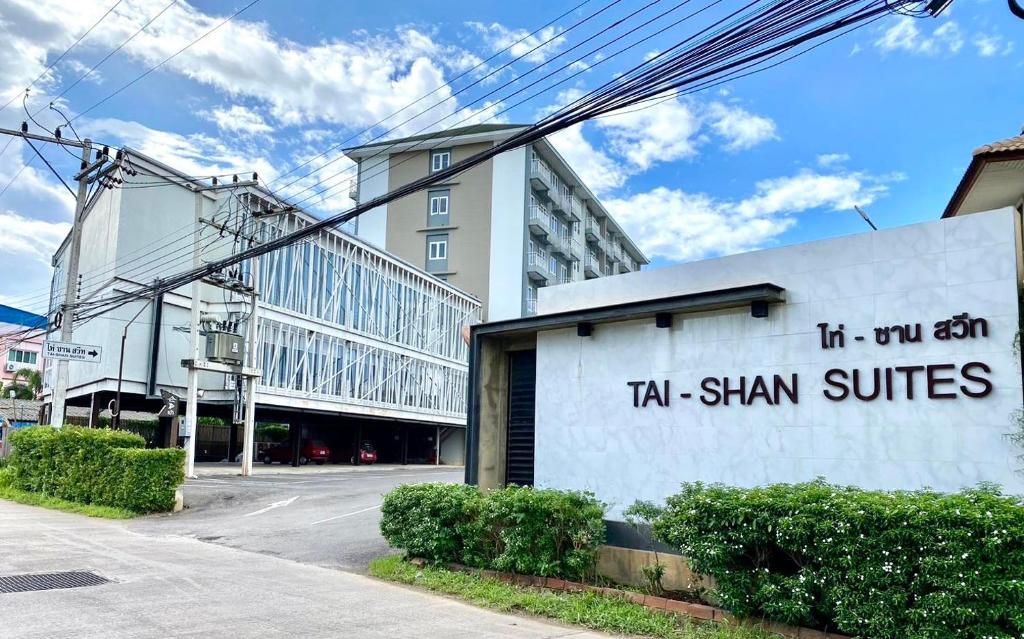 A hotel entrance with a sign reading 'Tai-Shan Suites' and a modern building in the background.