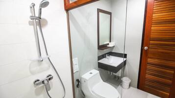 A bathroom with a glass-enclosed shower, a white toilet, a sink with a mirror above it, and a wooden door.