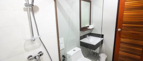 Un baño con ducha envuelta en vidrio, inodoro blanco, lavamanos con espejo y puerta de madera.