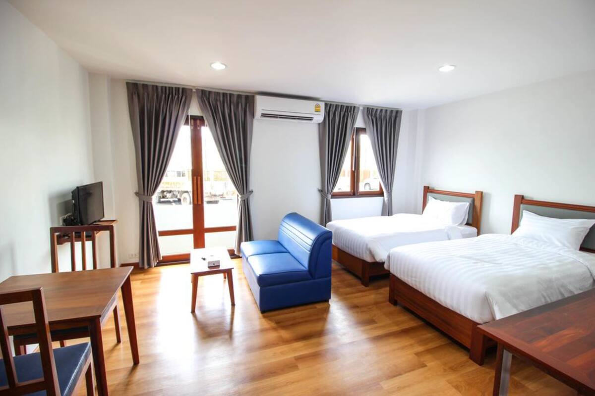A hotel room with two beds, a blue sofa, a wooden table, and a TV.