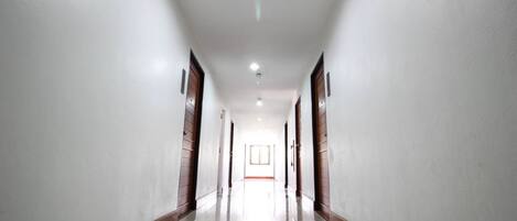 Un long couloir étroit aux murs blancs et aux boiseries, qui mène à une porte au fond.